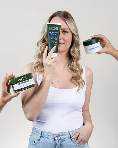 Moteris, laikanti Luxéol plaukų priežiūros priemones neutraliame fone