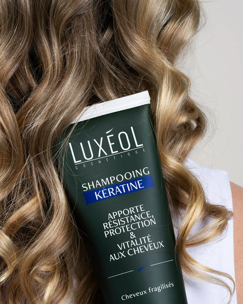Luxéol šampūno su keratinu buteliukas su banguotais plaukais fone